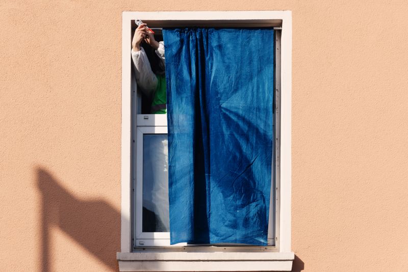 Detailaufnahme eines Fensters. Blaue Cyanotypie wird in den Fensterrahmen eingepasst.  Zwei Hände befestigen die Stange mithilfe einer Zange.
