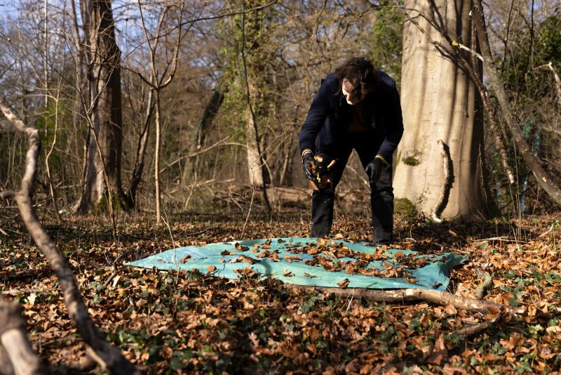 Dico Kruijsse scatters leaves on the fabric lying on the ground.
